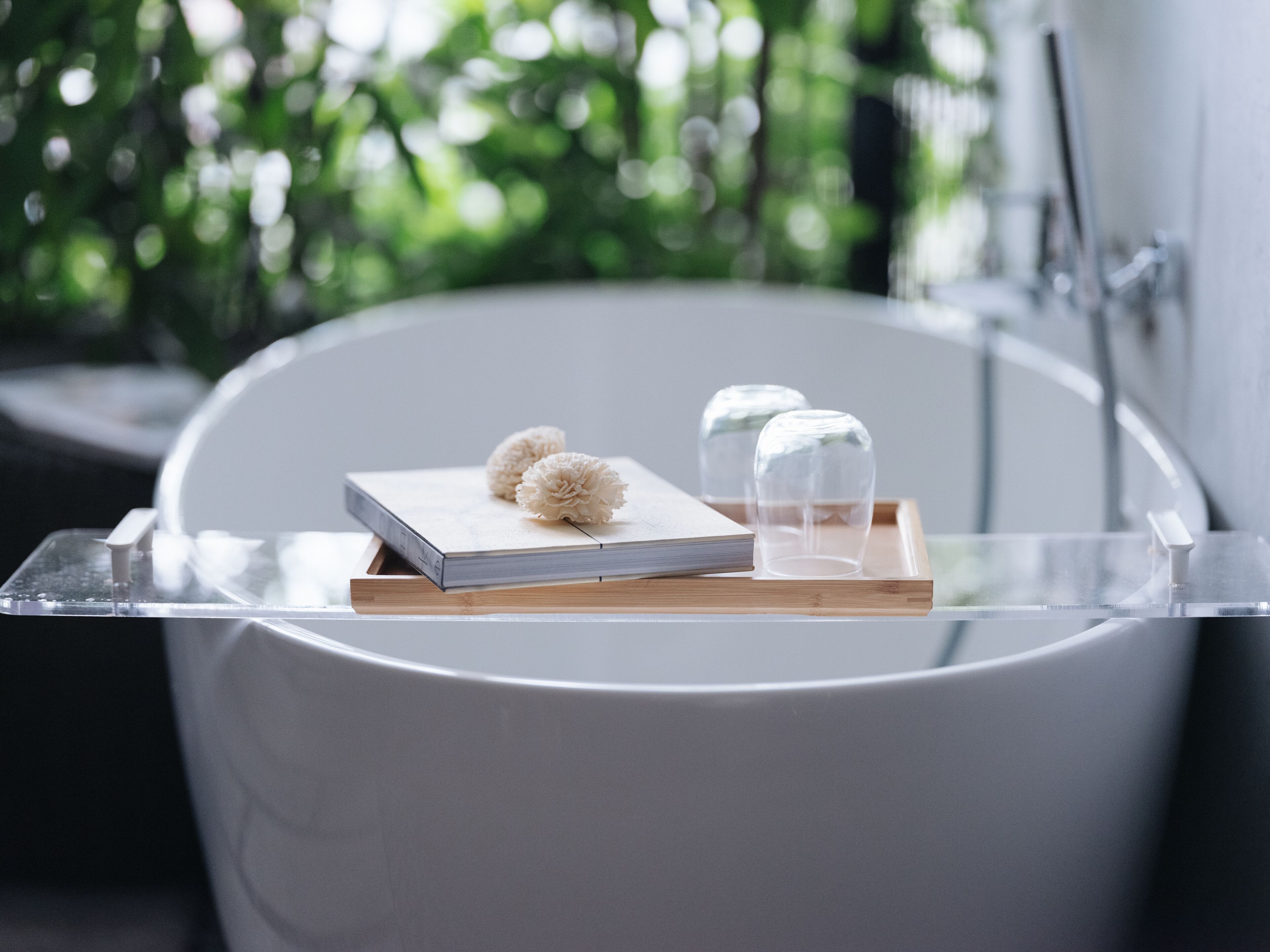 Una bañera con una bandeja de madera que sostiene un libro y dos productos de baño blancos.