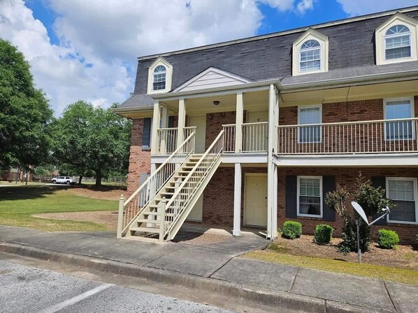 A two-story building with a covered front porch, a staircase, and a satellite dish.