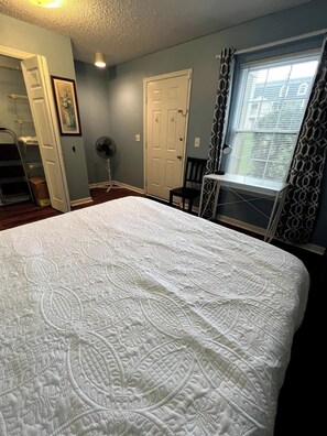 Un dormitorio con una cama grande, una puerta, un ventilador y una ventana con cortinas estampadas.