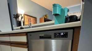 A modern kitchen with a stainless steel dishwasher, wooden cabinets, and a wooden floor. - AU Condo Getaway Across From Vet School - Kitchen, Pools, Queen BR, Pets Welcome (Auburn)