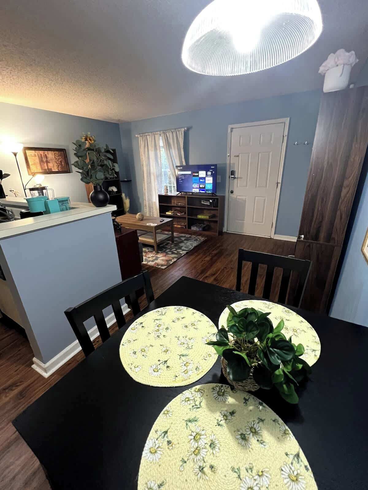 A dining area with a black table and chairs, a floral table runner, and a potted plant.
