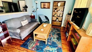 A living room with a grey sofa, a wooden coffee table, a blue patterned rug, a bookshelf, and a television. - AU Condo Getaway Across From Vet School - Kitchen, Pools, Queen BR, Pets Welcome (Auburn)