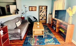 A living room with a grey sofa, a wooden coffee table, a bookshelf, a TV stand, and a colorful rug. - AU Condo Getaway Across From Vet School - Kitchen, Pools, Queen BR, Pets Welcome (Auburn)