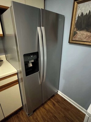 A stainless steel refrigerator with a water dispenser, located in a kitchen with wooden flooring and a light blue wall. - AU Condo Getaway Across From Vet School - Kitchen, Pools, Queen BR, Pets Welcome (Auburn)