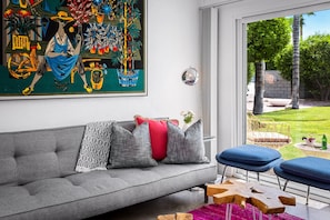 Um sofá cinzento com almofadas estampadas, uma mesa de centro de madeira e um quadro abstrato vibrante acima do sofá.