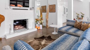 Een moderne woonkamer met een open haard, een blauwe gestreepte bank en een groot vloerkleed.
