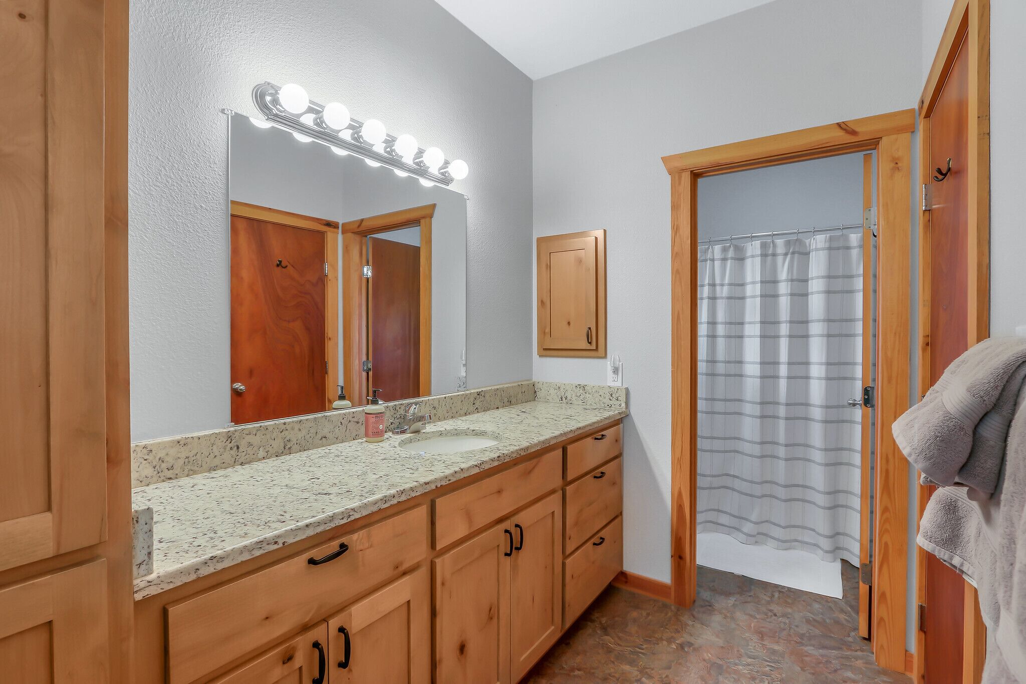 A bathroom with a vanity, a mirror with lights, a shower curtain, and wooden doors.