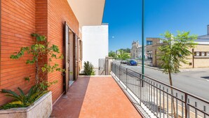 A balcony with a red brick wall, a white wall, and a metal railing overlooking a street with cars and buildings. - 3611 Casa di Paolo by Barbarhouse (Campi Salentina)