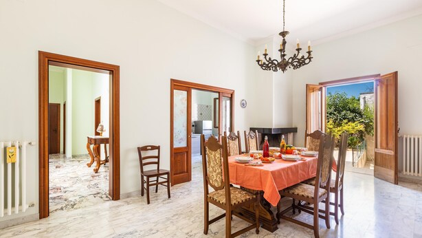 A dining area with a marble floor, wooden chairs, a table with a red tablecloth, and a chandelier. - 3611 Casa di Paolo by Barbarhouse (Campi Salentina)