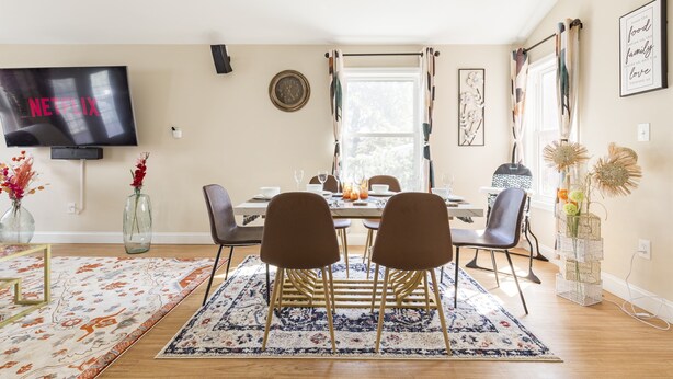 A dining area with a TV displaying 'NETFLIX', a clock, and a window with curtains.