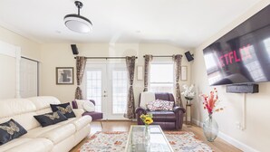 A living room with a sofa, armchair, coffee table, and a TV mounted on the wall.