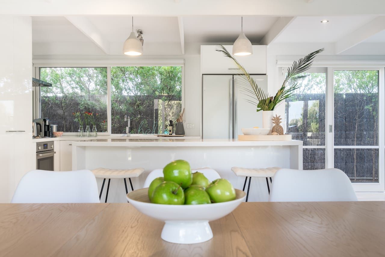 A modern kitchen with a central island, white cabinetry, and a bowl of green apples on the table.