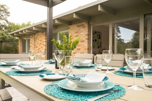 An outdoor dining area with a long table set for a meal, surrounded by chairs and a brick wall.
