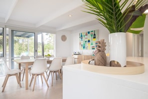 A modern dining area with a large window, a clock on the wall, and a plant in a white vase.