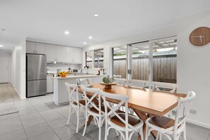 A modern kitchen with white cabinetry, a stainless steel refrigerator, and a dining area with a wooden table and white chairs.