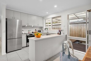 A modern kitchen with white cabinetry, a stainless steel refrigerator, and a central island with a bowl of fruit.