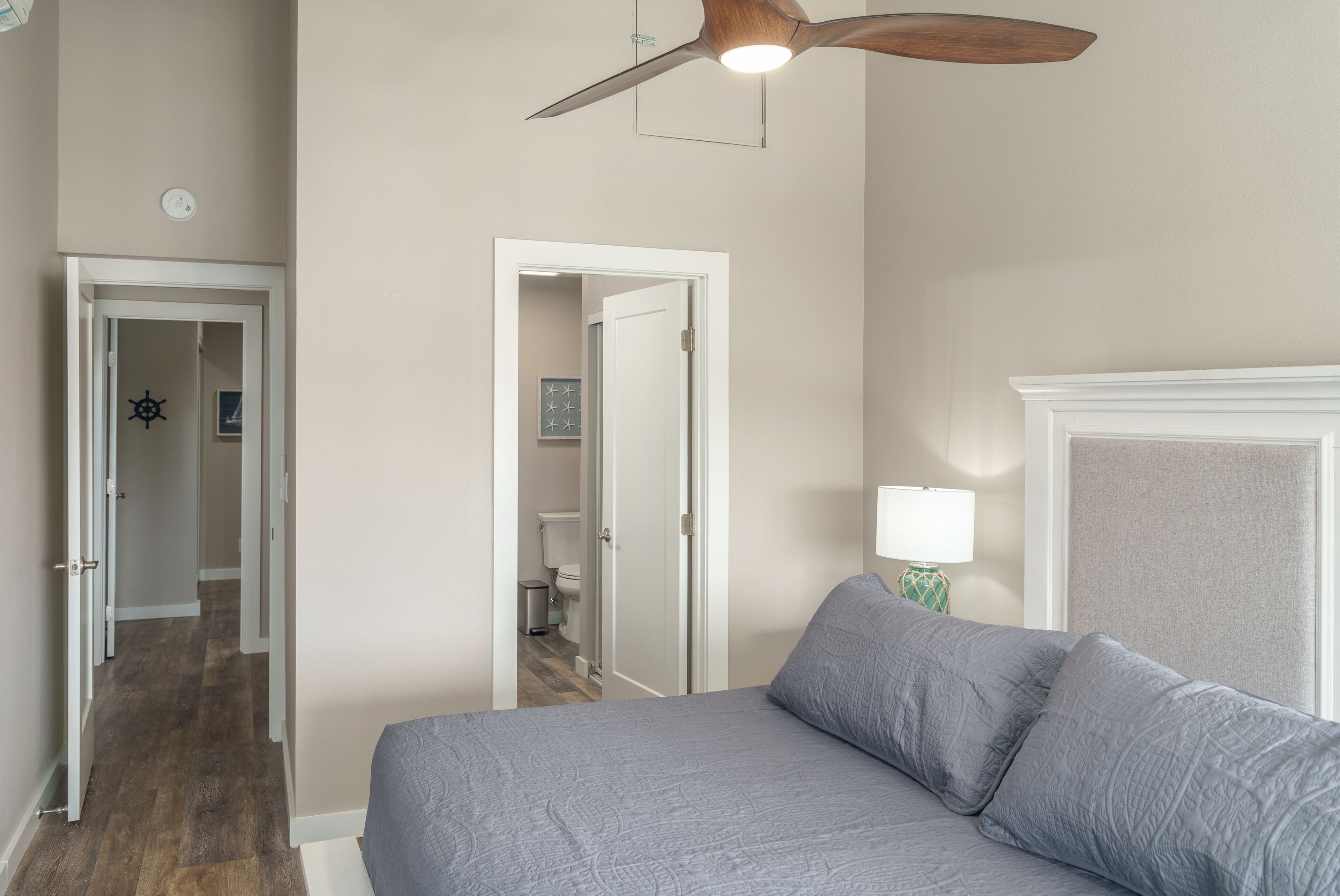 Een slaapkamer met een bed, een plafondventilator en een deur naar een badkamer.