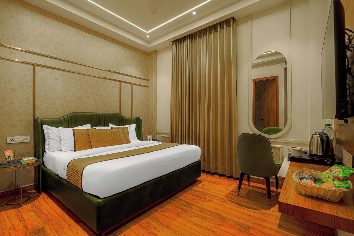 A hotel room with a large bed, a desk, a chair, a mirror, and a window with curtains.