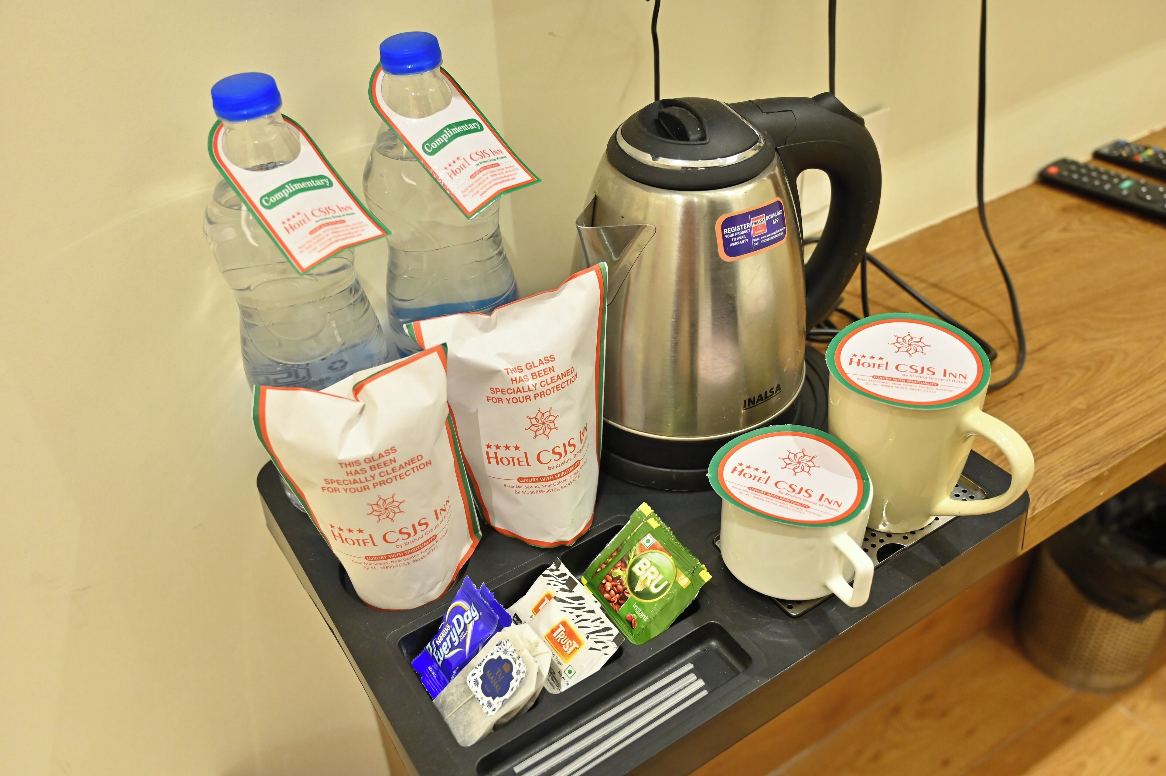 A tray with bottled water, a kettle, a mug, and some snacks.