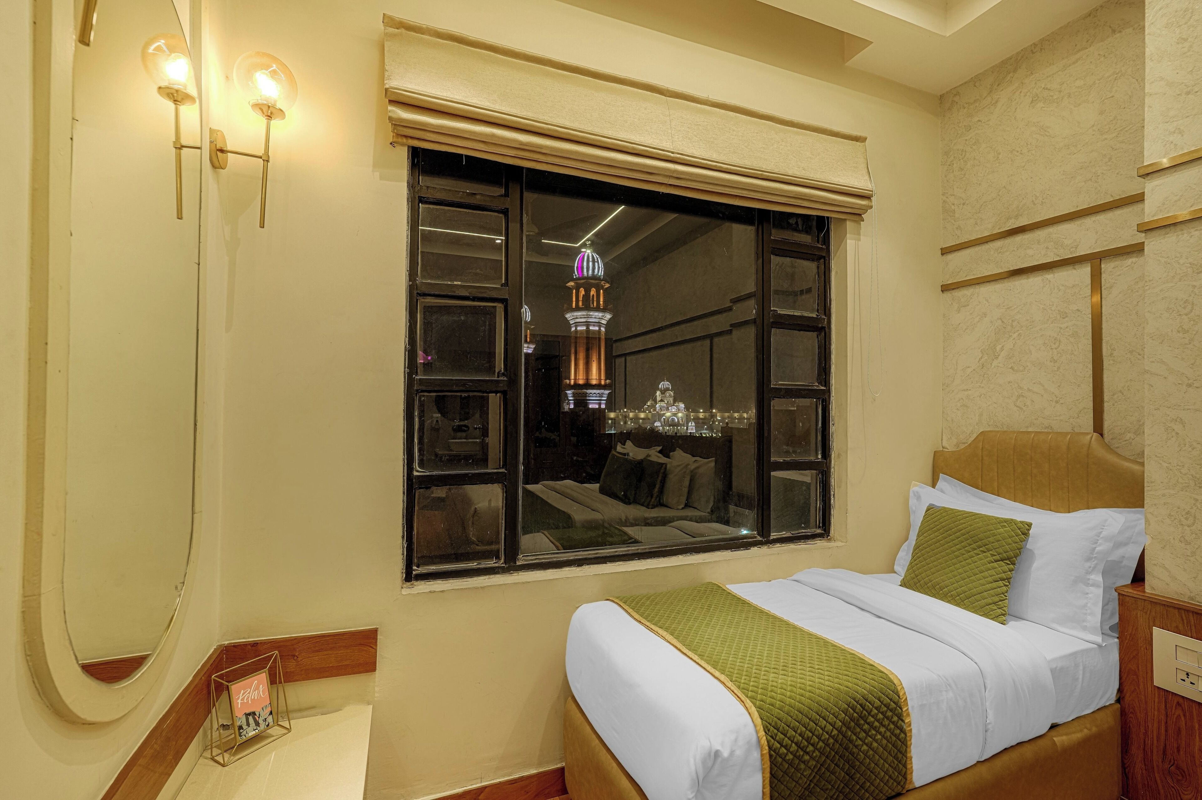 A hotel room with a bed, a window with a view of a building, and wall-mounted lights.