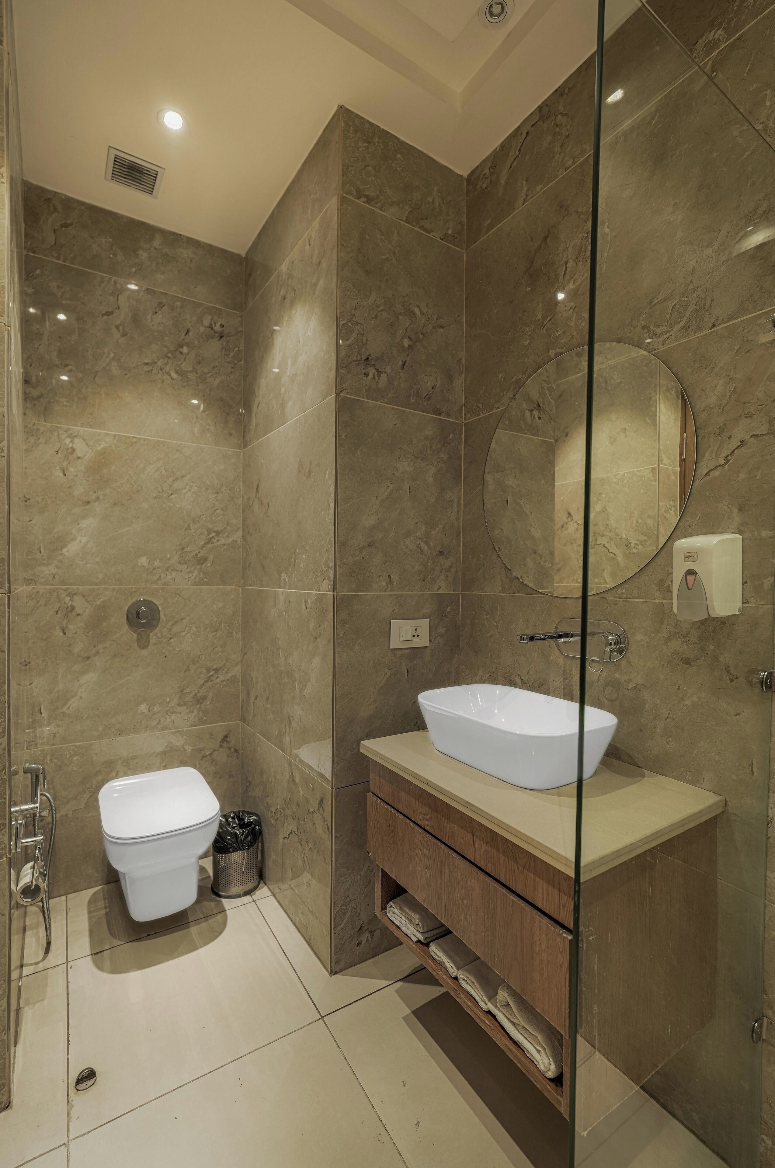 A modern bathroom with a glass-enclosed shower, a white vessel sink, and a marble-tiled wall.