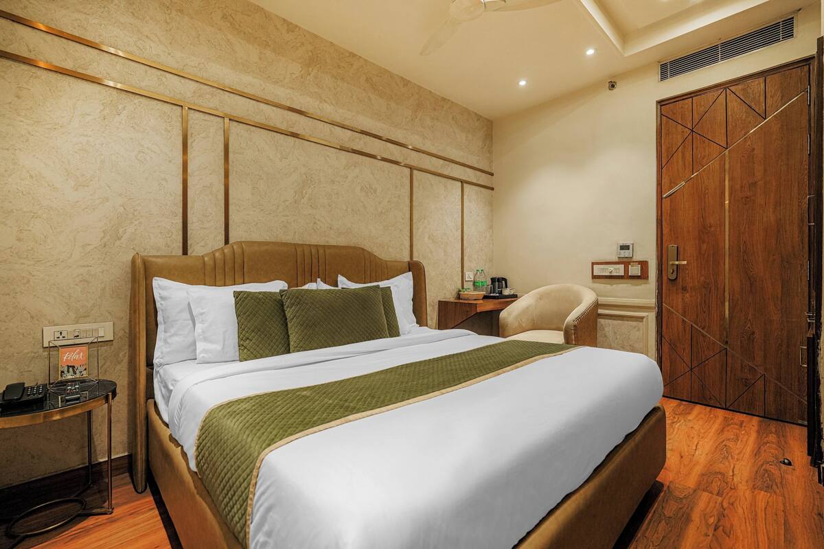 A neatly made bed with a green throw, a wooden headboard, and a bedside table with a phone and a lamp.