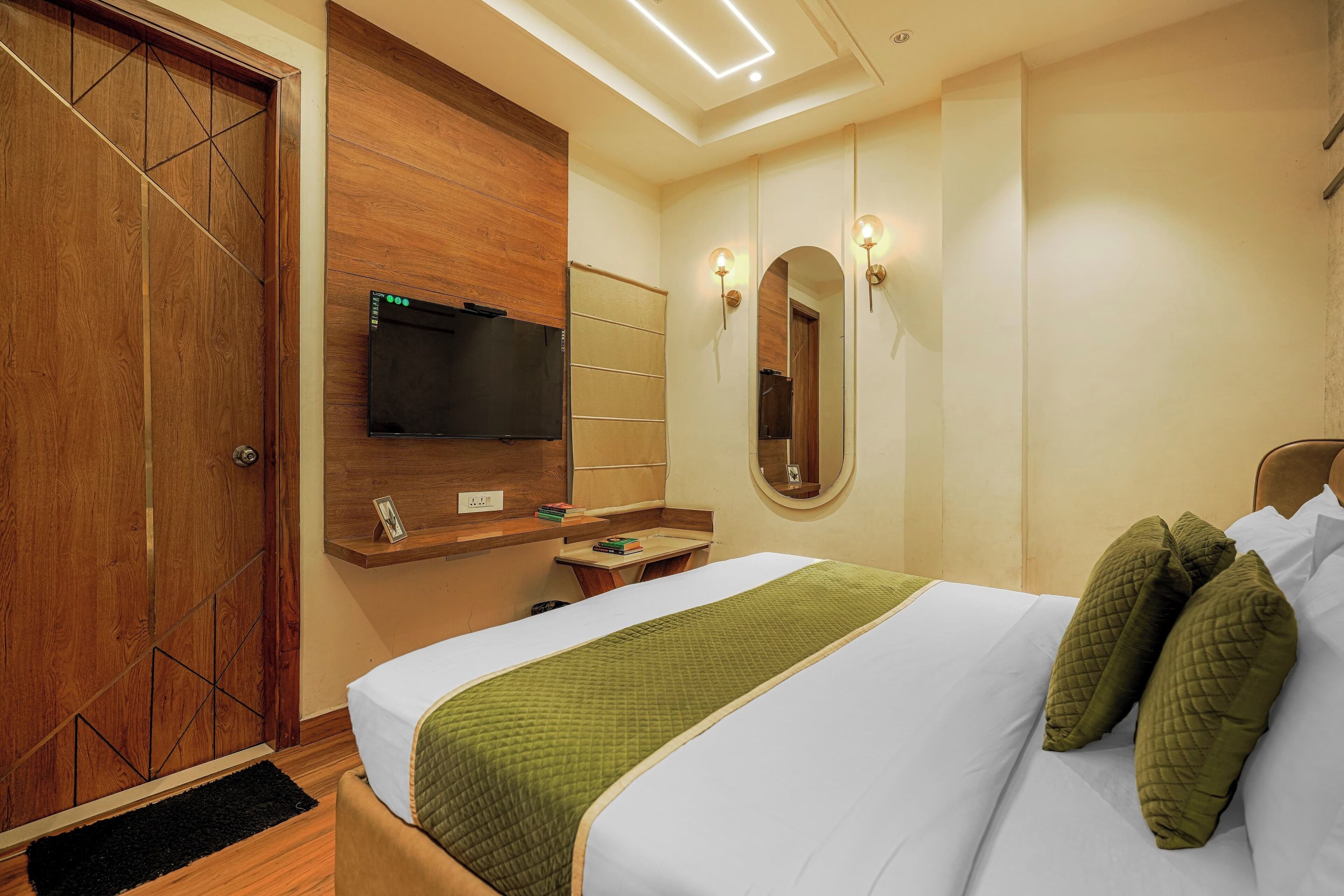 Une chambre d’hôtel comprenant un lit, une armoire en bois, un téléviseur fixé au mur, un miroir et une petite table avec une étagère.