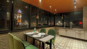 Un coin repas avec une table dressée pour deux personnes, de grandes fenêtres offrant une vue sur la ville et un plafond en bois.