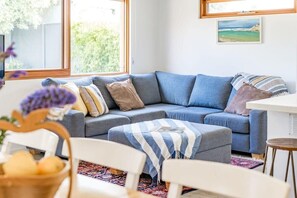 A living room with a grey sectional sofa, a white coffee table, and a view of greenery outside.
