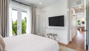 Un dormitorio con cama, televisión montada en la pared y balcón con cortinas.
