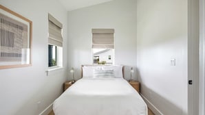 Un dormitorio con una cama grande, dos mesitas de noche, una ventana con persianas y un cuadro enmarcado en la pared.