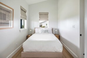 A bedroom with a large bed, two bedside tables, a window with blinds, and a framed picture on the wall.