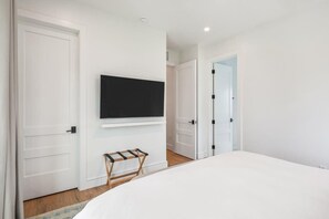 A bedroom with a bed, a TV mounted on the wall, and a door leading to another room. - The Windrose Estate at Lunara Bay (Key West)