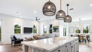 Una cocina moderna con una isla grande, iluminación colgante y un comedor con mesa y sillas.
