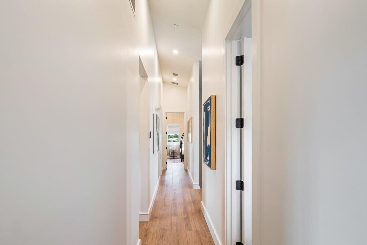 A hallway with white walls, wooden flooring, and framed pictures on the walls.