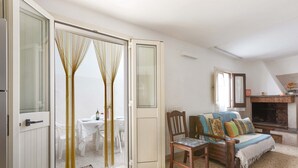Eine offene Schiebetür führt in einen Essbereich mit Tisch und Stühlen, einem Sofa mit Kissen sowie einem Kamin.