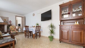 Ein Wohnzimmer mit Esstisch, Stühlen, Fernseher, Schrank und einer Zimmerpflanze.