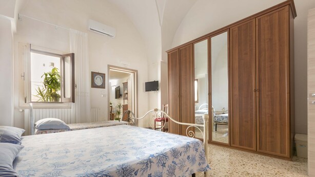 Ein Schlafzimmer mit Bett, Kleiderschrank, Spiegel und einem Fenster mit Vorhängen.