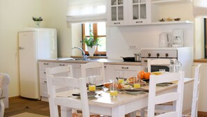 A kitchen with white cabinets, a refrigerator, and a dining table with chairs. There is a window with a plant on the windowsill. - Villa Danica ZadarVillas (Sukošan)
