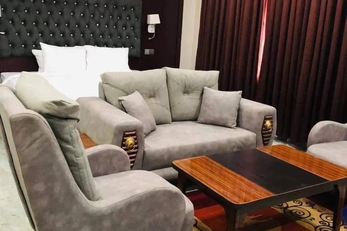 A hotel room with a tufted headboard, a grey sofa set, a wooden coffee table, and a patterned rug.