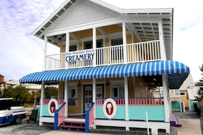 A creamery with a blue and white striped awning, a signboard, and a staircase leading to the entrance.