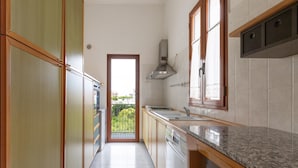 A narrow kitchen with wooden cabinets, a stainless steel range hood, and a view through a door to a balcony. - 3606 Dimora Incantevole by Barbarhouse (Lecce)
