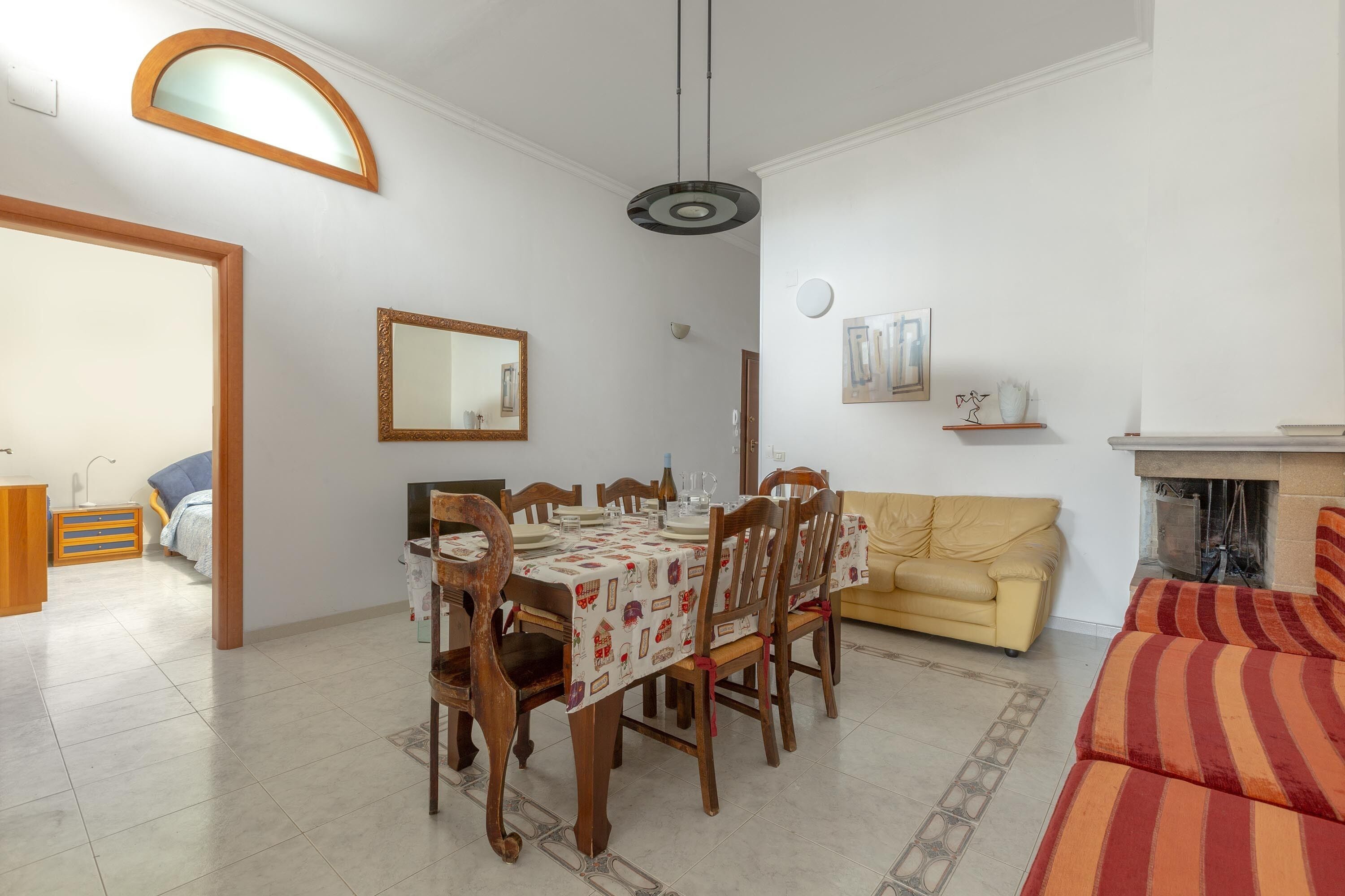 A dining area with a table set for four, surrounded by wooden chairs, a sofa, and a fireplace.