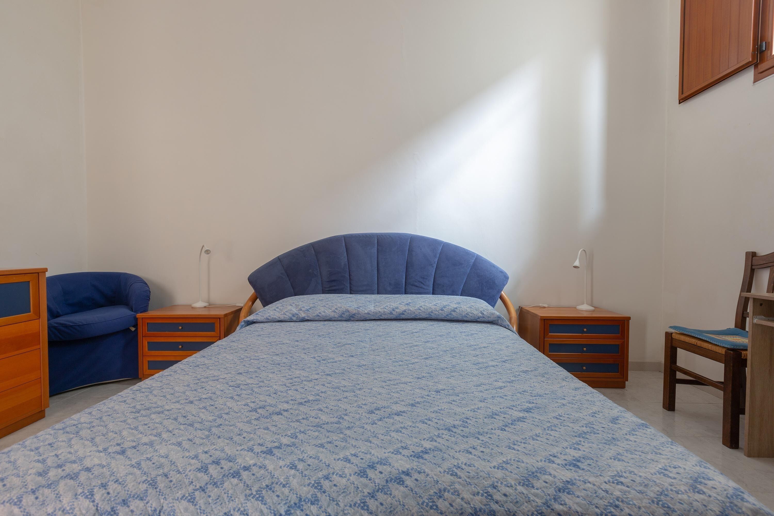 Ein Schlafzimmer mit einem Bett, zwei Nachttischen, einem Sessel und einem Kleiderschrank.