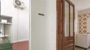 Een hal met een rood tapijt, een houten deur, een witte muur en een betegelde muur met een geometrisch patroon.
