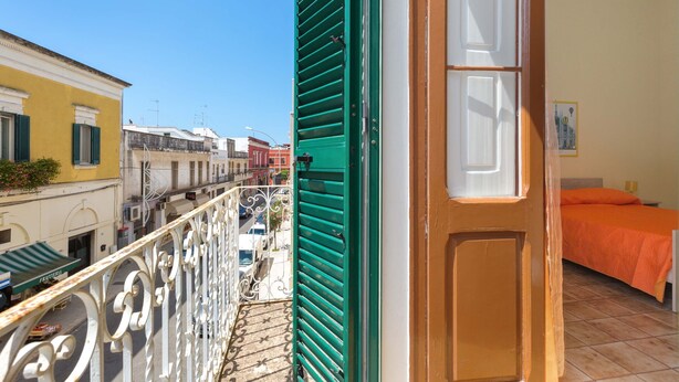 Een balkon met een metalen hekwerk, een groene deur en een bed met een oranje sprei.