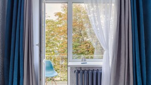 A room with a view of autumn trees through a window, a radiator, and a blue chair. - Cozy apartment on Vera Khoruzhey street (Minsk)