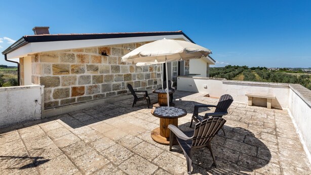 A stone building with a tiled patio, outdoor seating, and a view of the countryside.