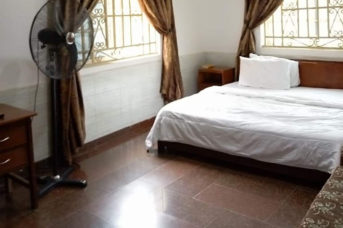 Une chambre d’hôtel avec un lit, une table de chevet, un ventilateur et des rideaux.