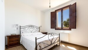 Un dormitorio con cama, mesita de noche, cómoda y ventana con contraventanas abiertas.